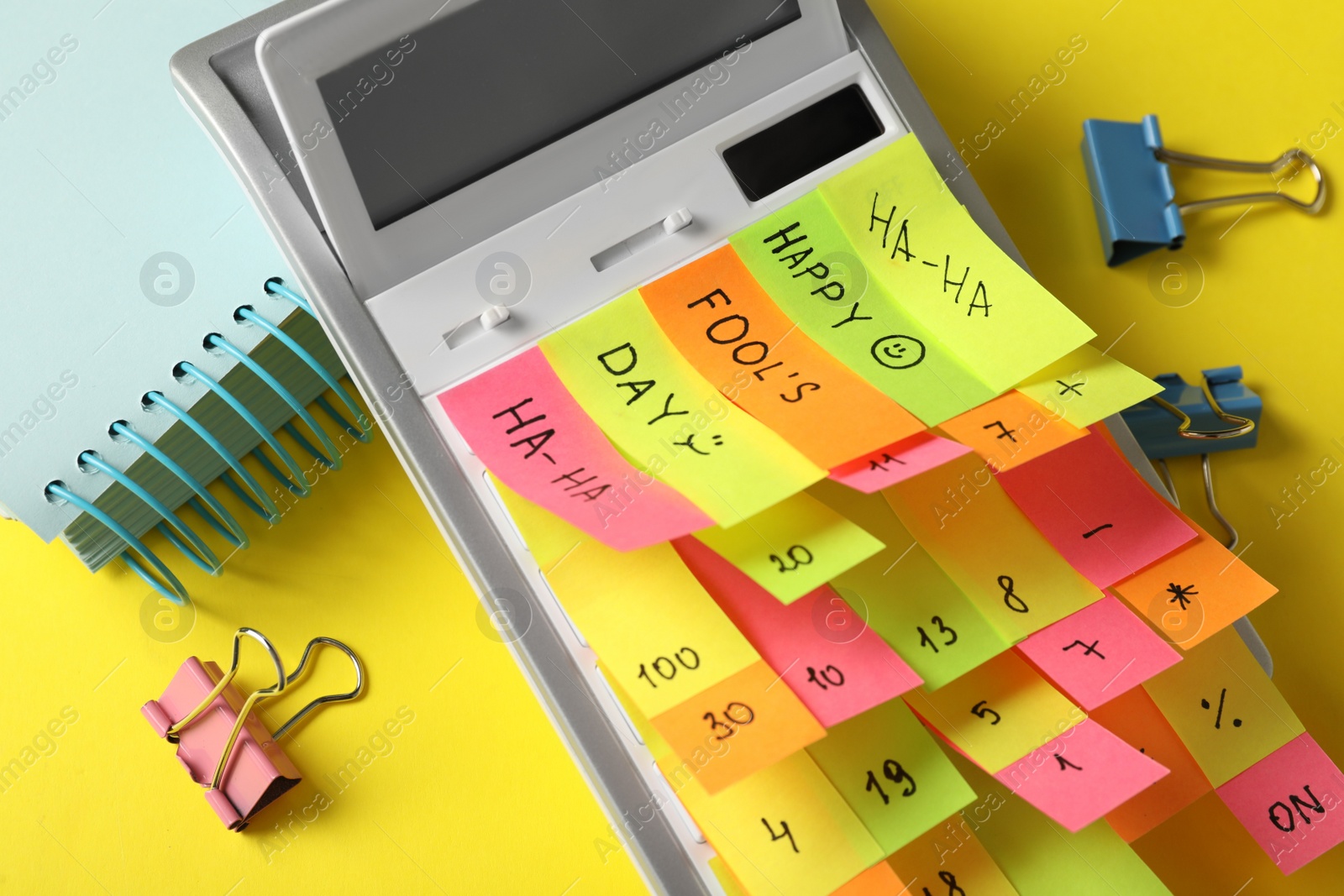 Photo of Calculator covered with stickers on yellow background, closeup. April fool's day