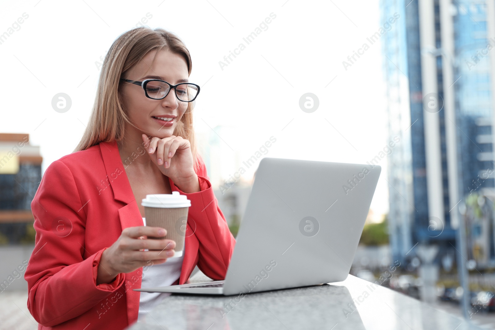 Photo of Beautiful businesswoman with laptop and cup of coffee in city