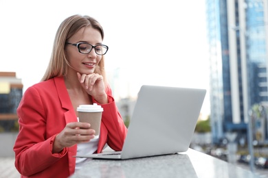 Photo of Beautiful businesswoman with laptop and cup of coffee in city