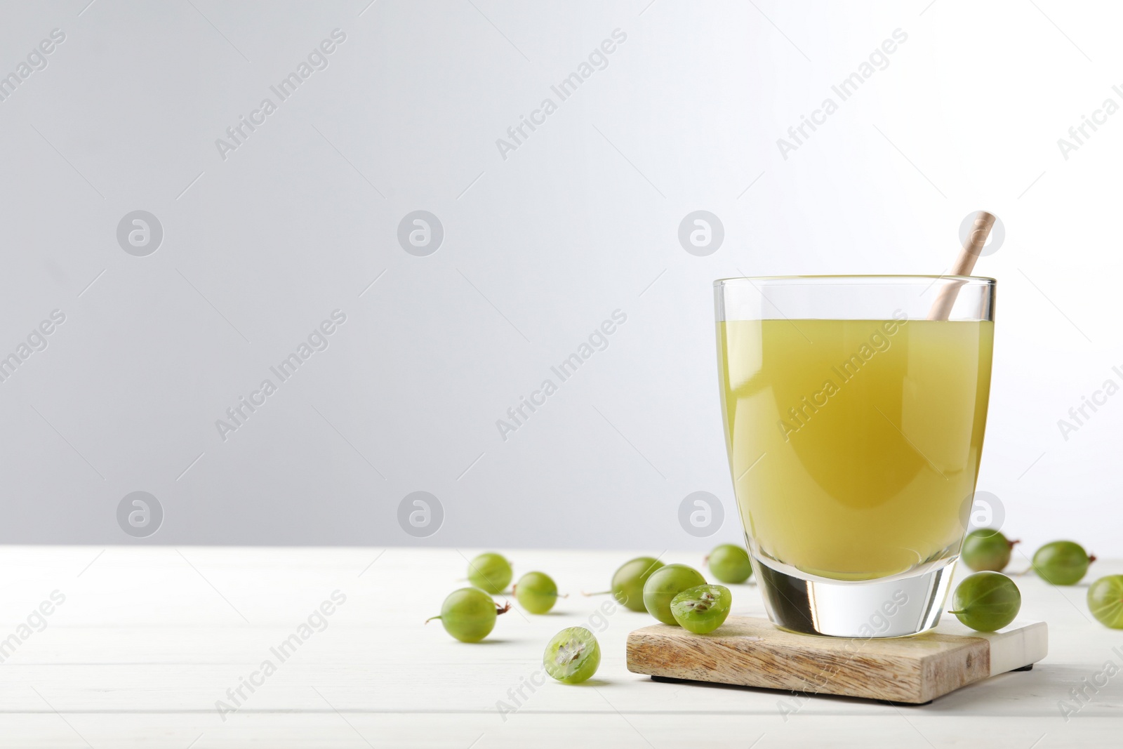 Photo of Tasty gooseberry juice on white wooden table against light background. Space for text