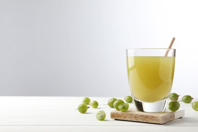 Tasty gooseberry juice on white wooden table against light background. Space for text