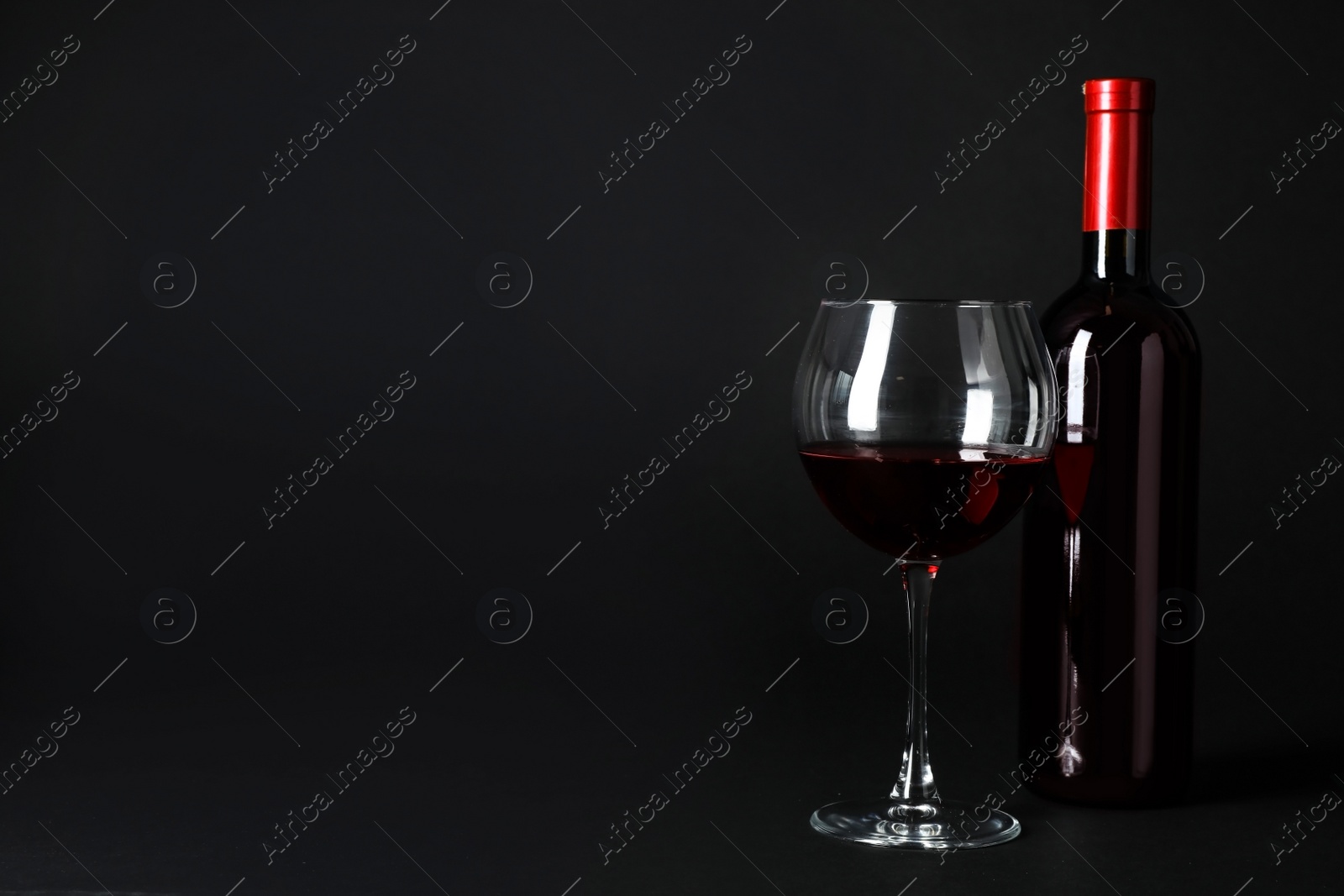 Photo of Bottle and glass of expensive red wine on dark background