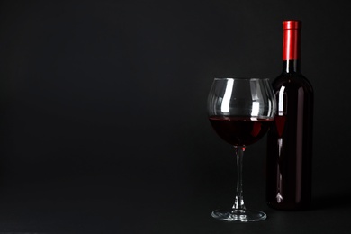 Photo of Bottle and glass of expensive red wine on dark background