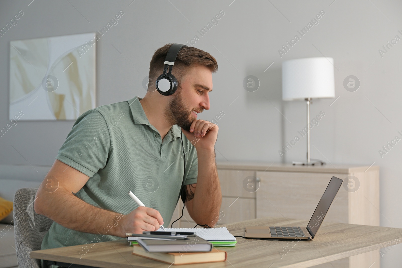 Photo of Young man taking notes during online webinar at table indoors