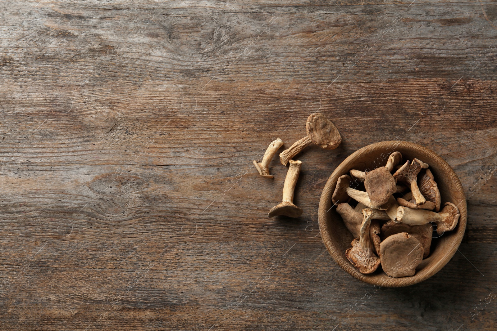 Photo of Bowl of dried mushrooms on wooden background, top view with space for text