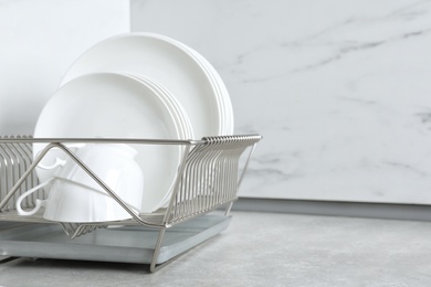 Drying rack with clean dishes and cups on table in kitchen. Space for text