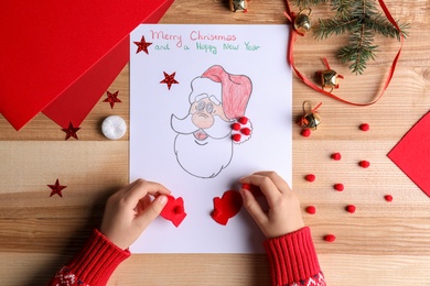 Photo of Little child making Christmas card at wooden table, top view