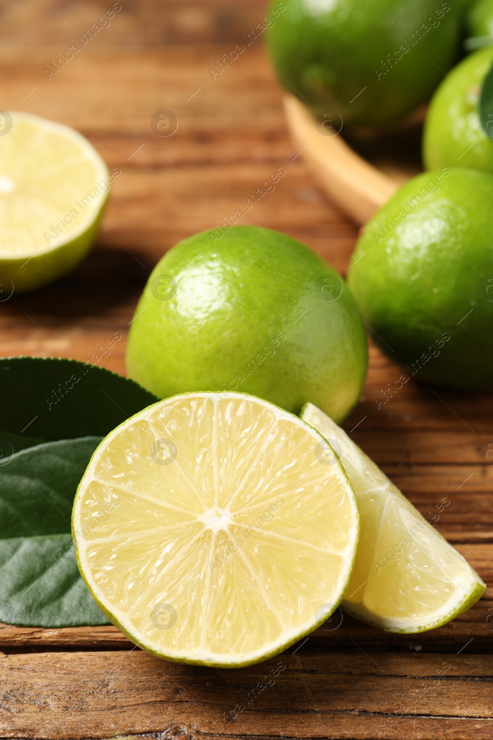 Photo of Fresh ripe limes and green leaves on wooden table, closeup