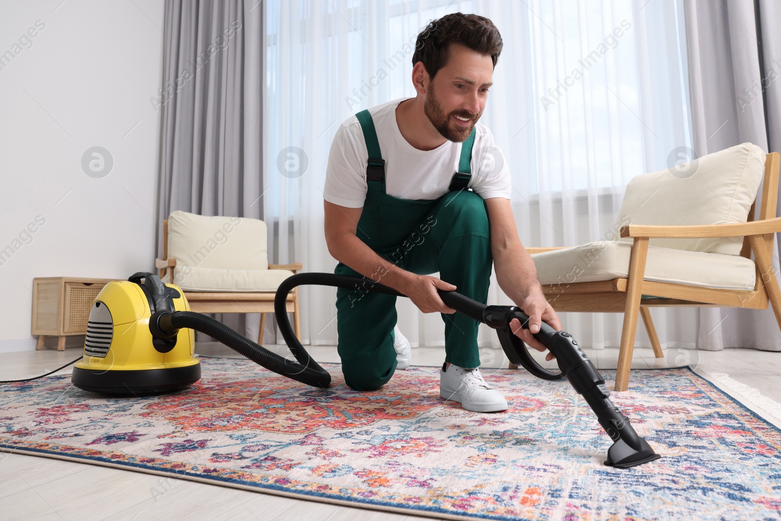 Photo of Dry cleaner's employee hoovering carpet with vacuum cleaner in room