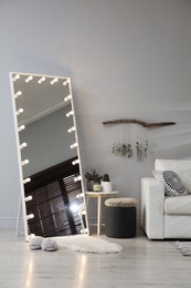 Photo of Stylish mirror with light bulbs and comfortable sofa in living room. Interior design