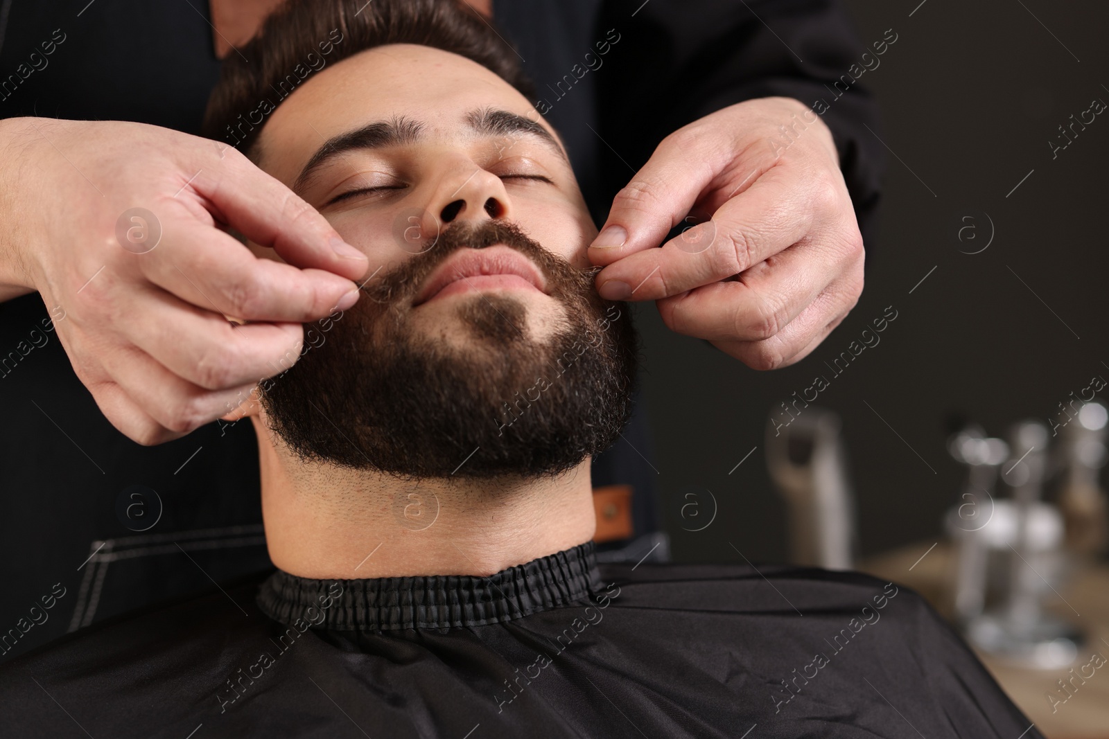 Photo of Professional barber working with client's mustache in barbershop, closeup