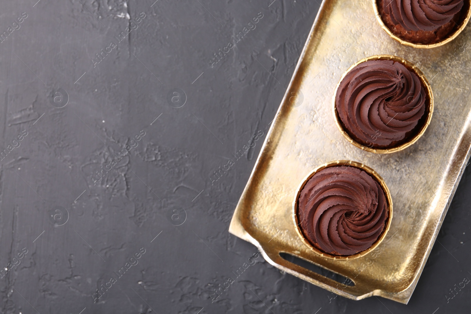 Photo of Delicious chocolate cupcakes on black textured table, top view. Space for text