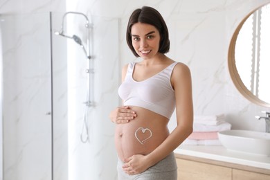 Photo of Young pregnant woman with cosmetic product on belly in bathroom