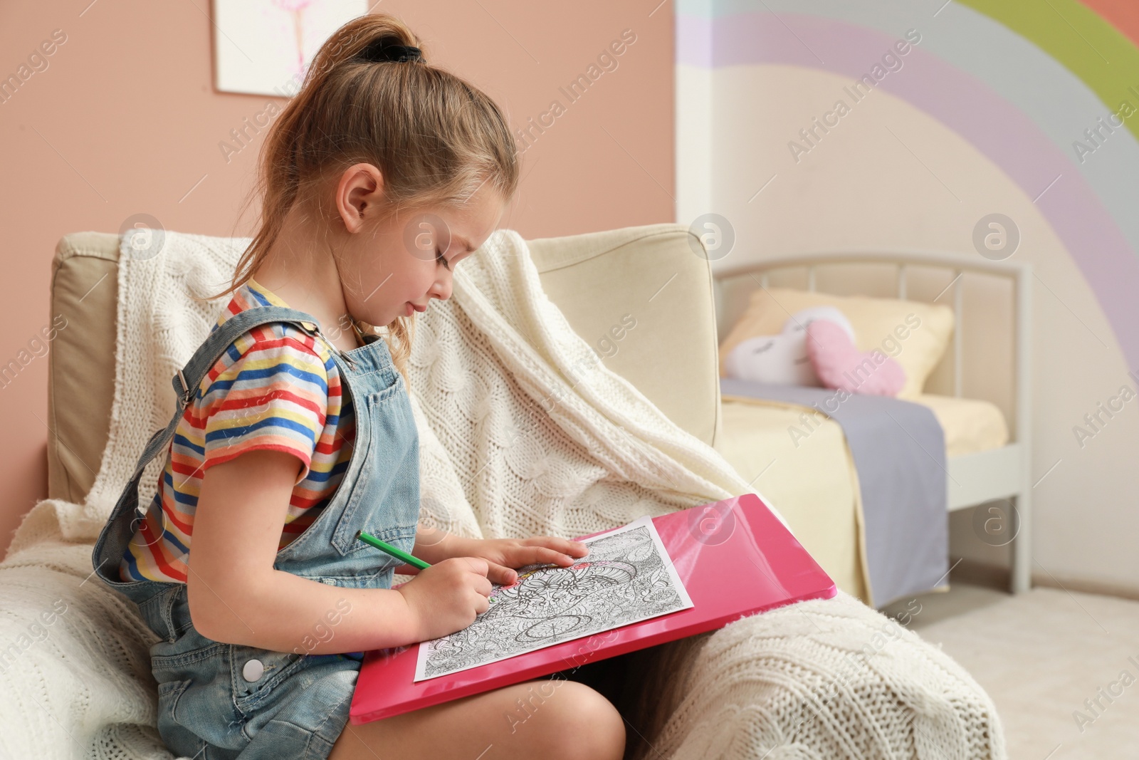 Photo of Little girl coloring antistress page in armchair indoors