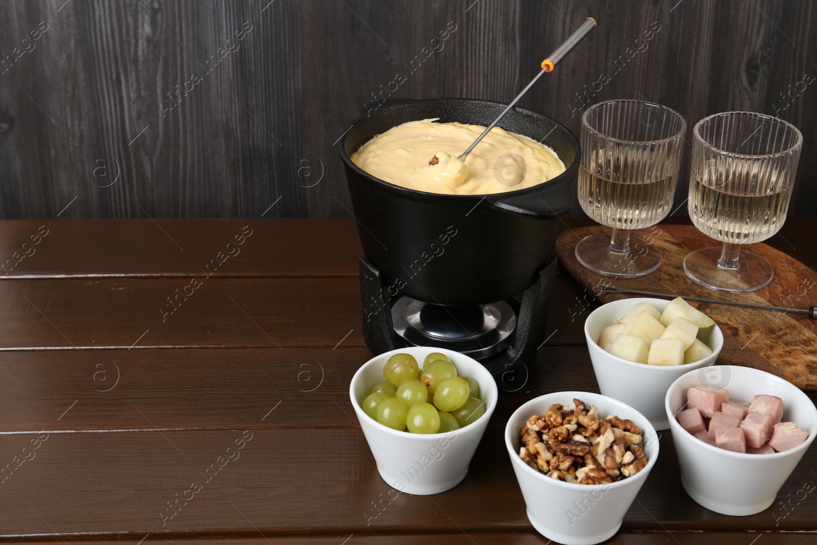 Photo of Fondue pot with tasty melted cheese, forks, wine and different snacks on wooden table, space for text