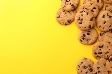 Photo of Many delicious chocolate chip cookies on yellow background, flat lay. Space for text