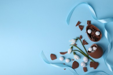 Flat lay composition with tasty broken chocolate eggs and beautiful decor on light blue background. Space for text
