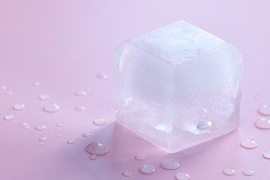 Photo of Crystal clear ice cube on light pink background, closeup. Space for text