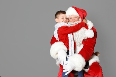 Photo of Little boy hugging authentic Santa Claus on grey background
