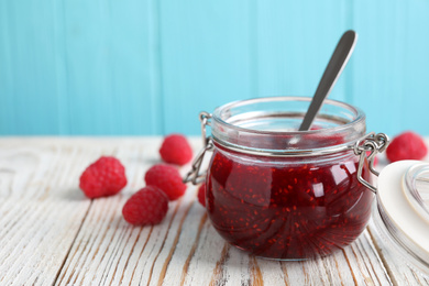 Delicious jam and fresh raspberries on white wooden table. Space for text