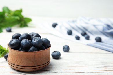 Wooden bowl with tasty blueberries on white table, space for text