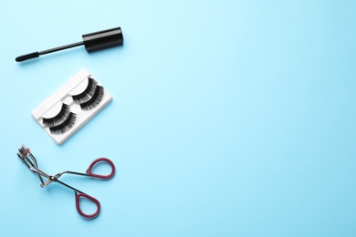 Photo of False eyelashes, curler and mascara on light blue background, flat lay. Space for text