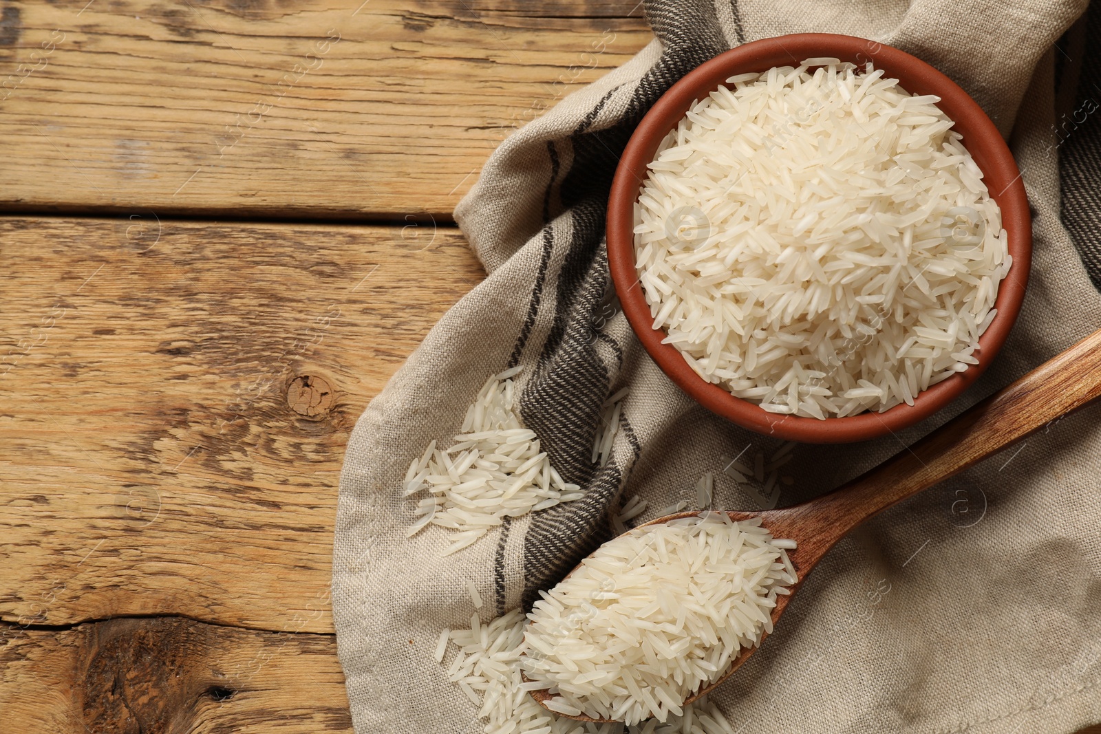 Photo of Raw basmati rice in bowl and spoon on wooden table, top view. Space for text