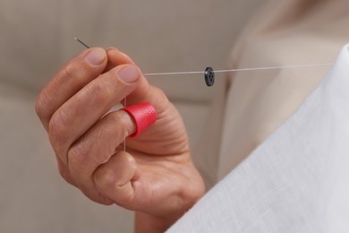 Photo of Woman sewing button with thimble and needle, closeup