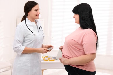 Overweight woman and nutritionist with digital caliper in clinic