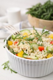 Cooked bulgur with vegetables in bowl on white wooden table, closeup