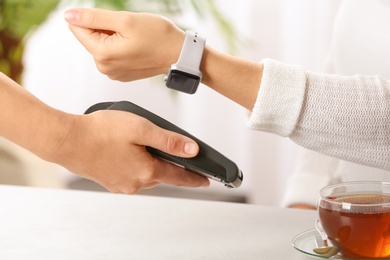 Woman using terminal for contactless payment with smart watch at table, closeup