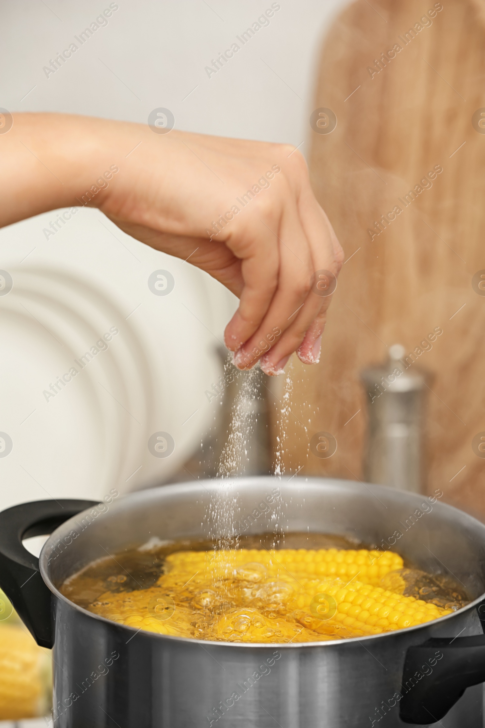 Photo of Woman salting water with corn cobs in stewpot, closeup