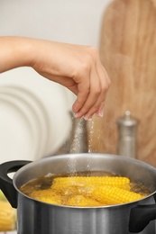 Photo of Woman salting water with corn cobs in stewpot, closeup