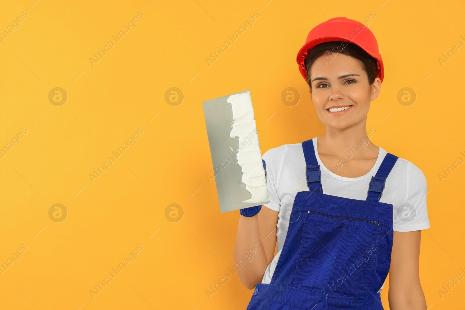 Photo of Professional worker with putty knife in hard hat on orange background, space for text