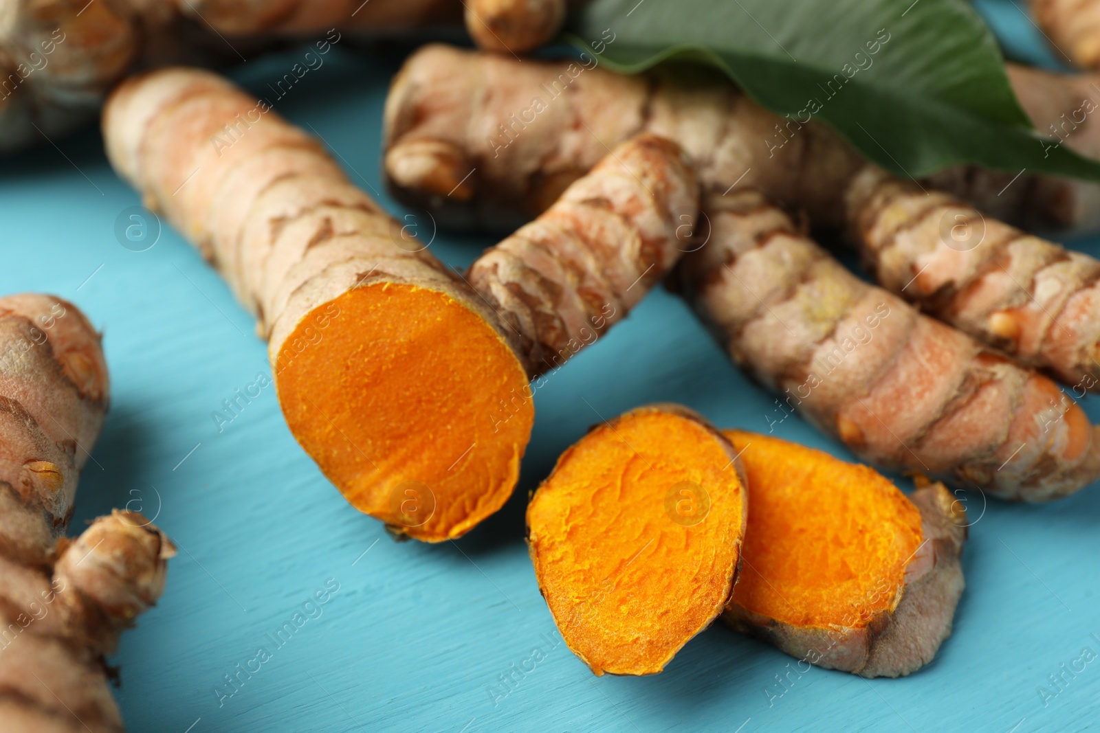 Photo of Whole and cut turmeric roots on light blue wooden table, closeup