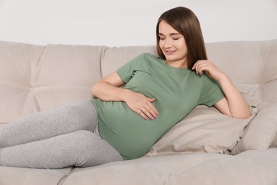 Photo of Happy pregnant woman lying on beige sofa indoors