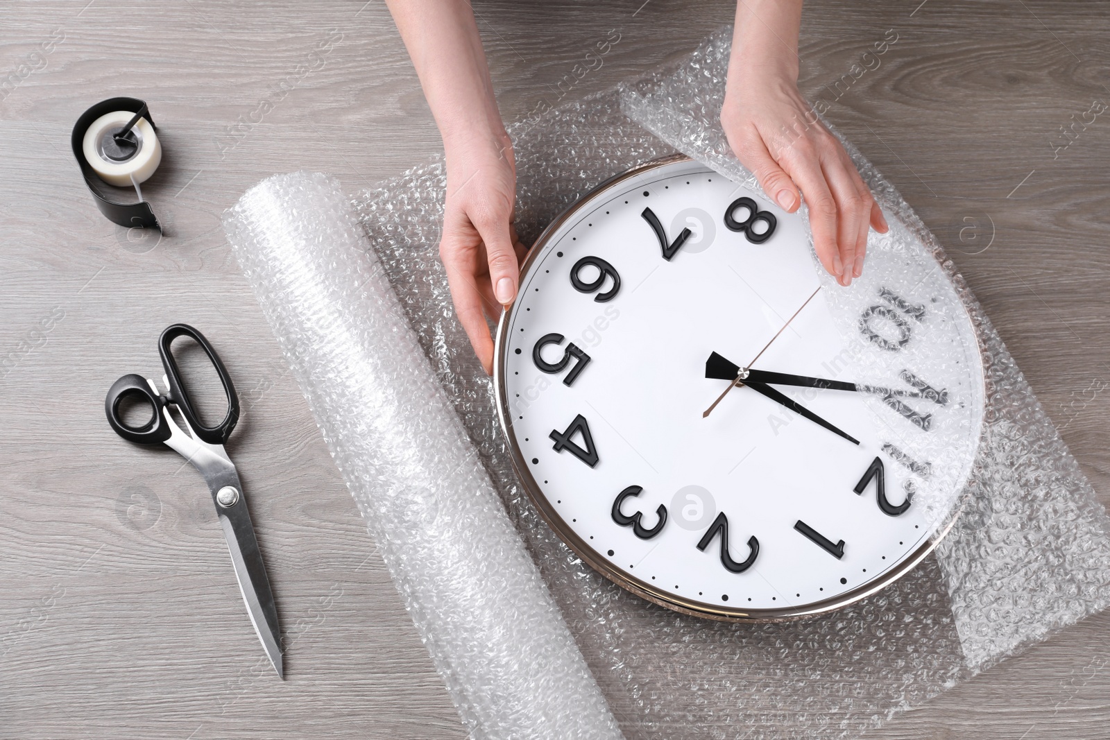 Photo of Woman covering wall clock with bubble wrap at wooden table, closeup
