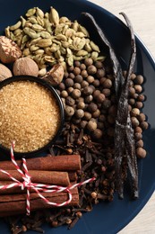 Plate with different aromatic spices on light wooden table, top view