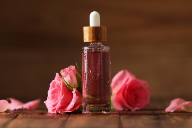 Photo of Bottle of essential rose oil and flowers on wooden table