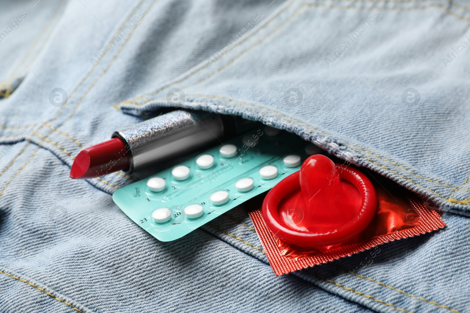 Photo of Red lipstick with condoms and birth control pills in pocket of jeans, closeup. Safe sex concept