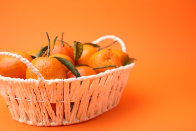 Photo of Fresh ripe tangerines and leaves in basket on orange table. Space for text