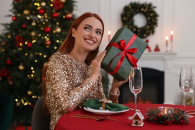 Photo of Beautiful young woman with Christmas gift at served table in room