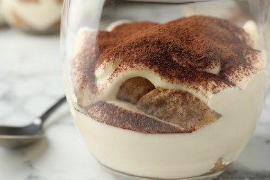 Delicious tiramisu in glass and spoon on white marble table, closeup