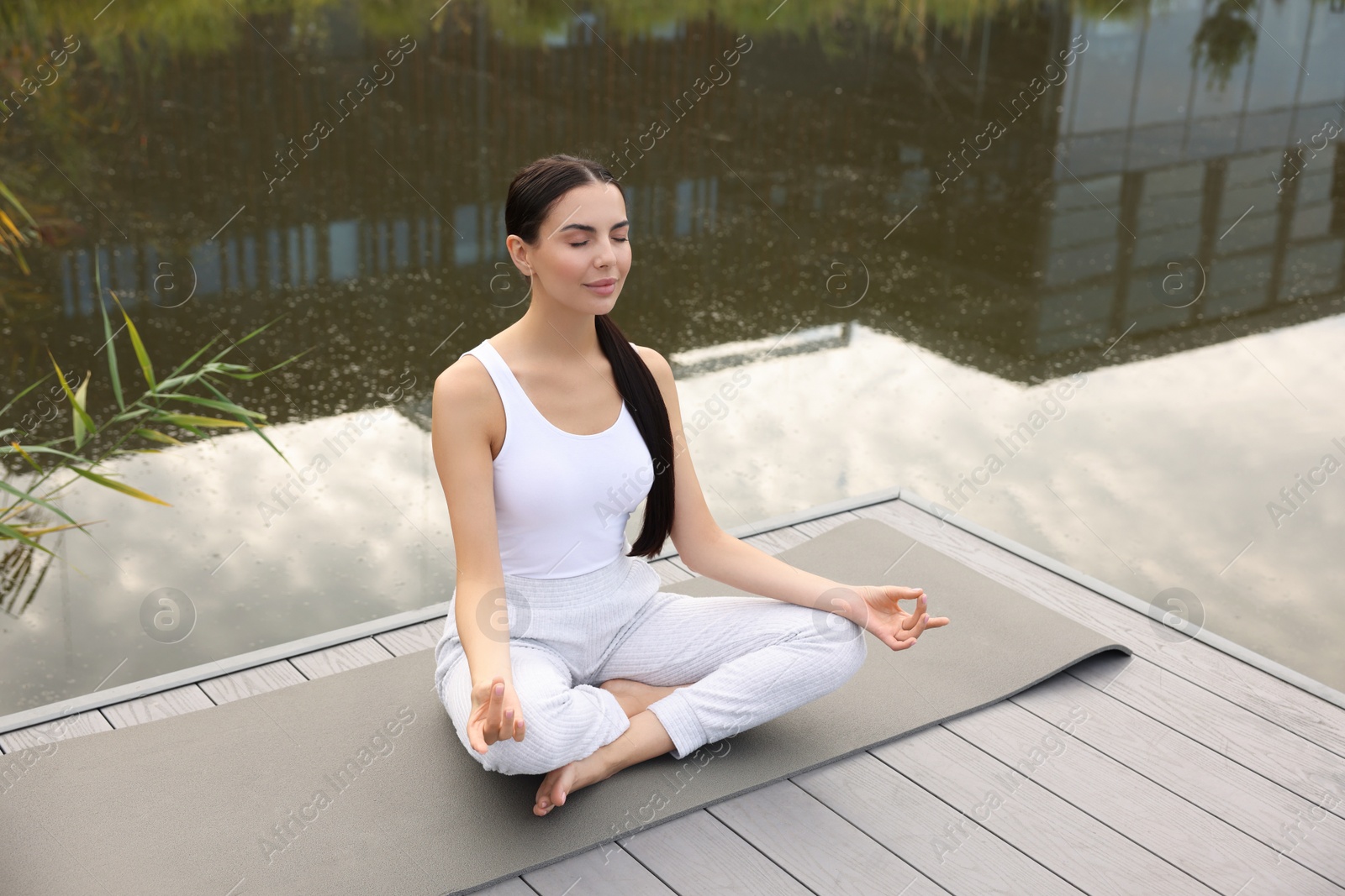 Photo of Beautiful young woman practicing Padmasana on yoga mat outdoors, above view. Lotus pose