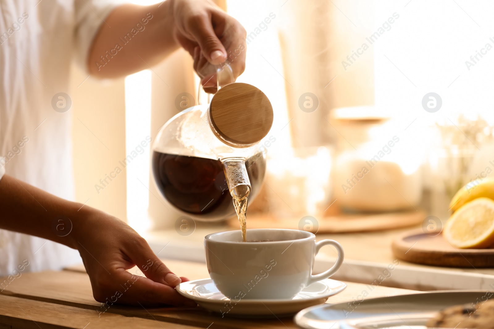 Photo of Woman pouring delicious tea into cup at wooden table, closeup