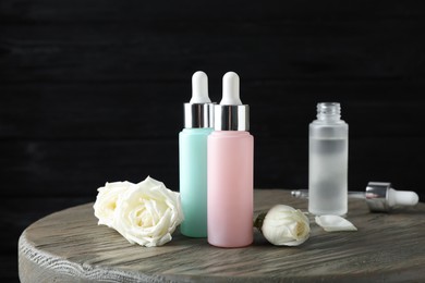 Photo of Bottles of serum and flowers on wooden table. Cosmetic products