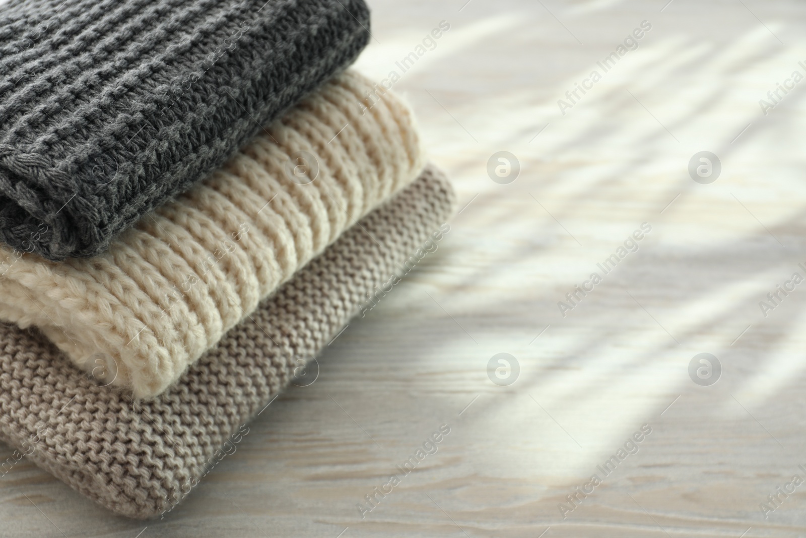 Photo of Stack of knitted scarfs on wooden table, space for text