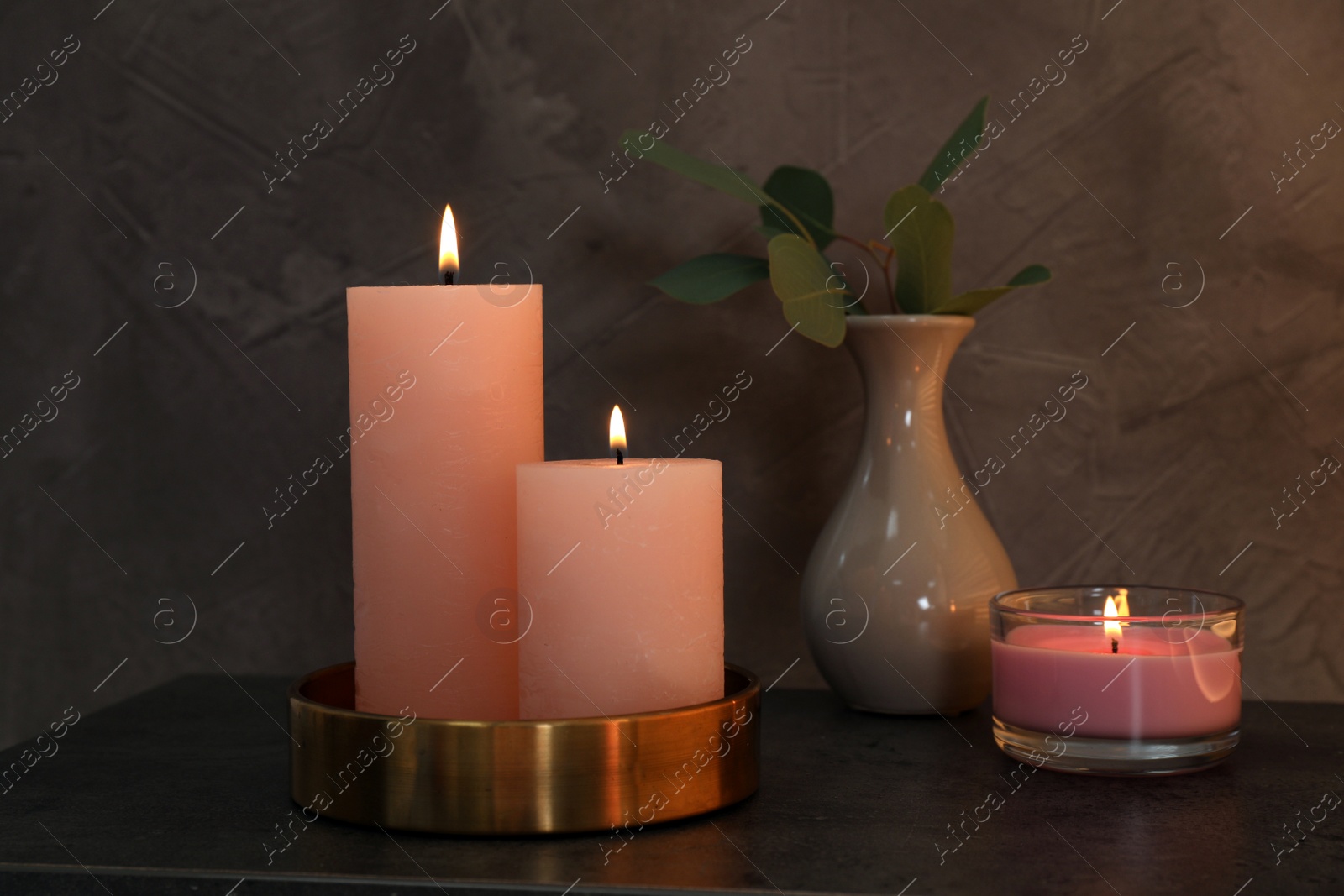 Photo of Scented candles near vase with eucalyptus branch on table in dark room