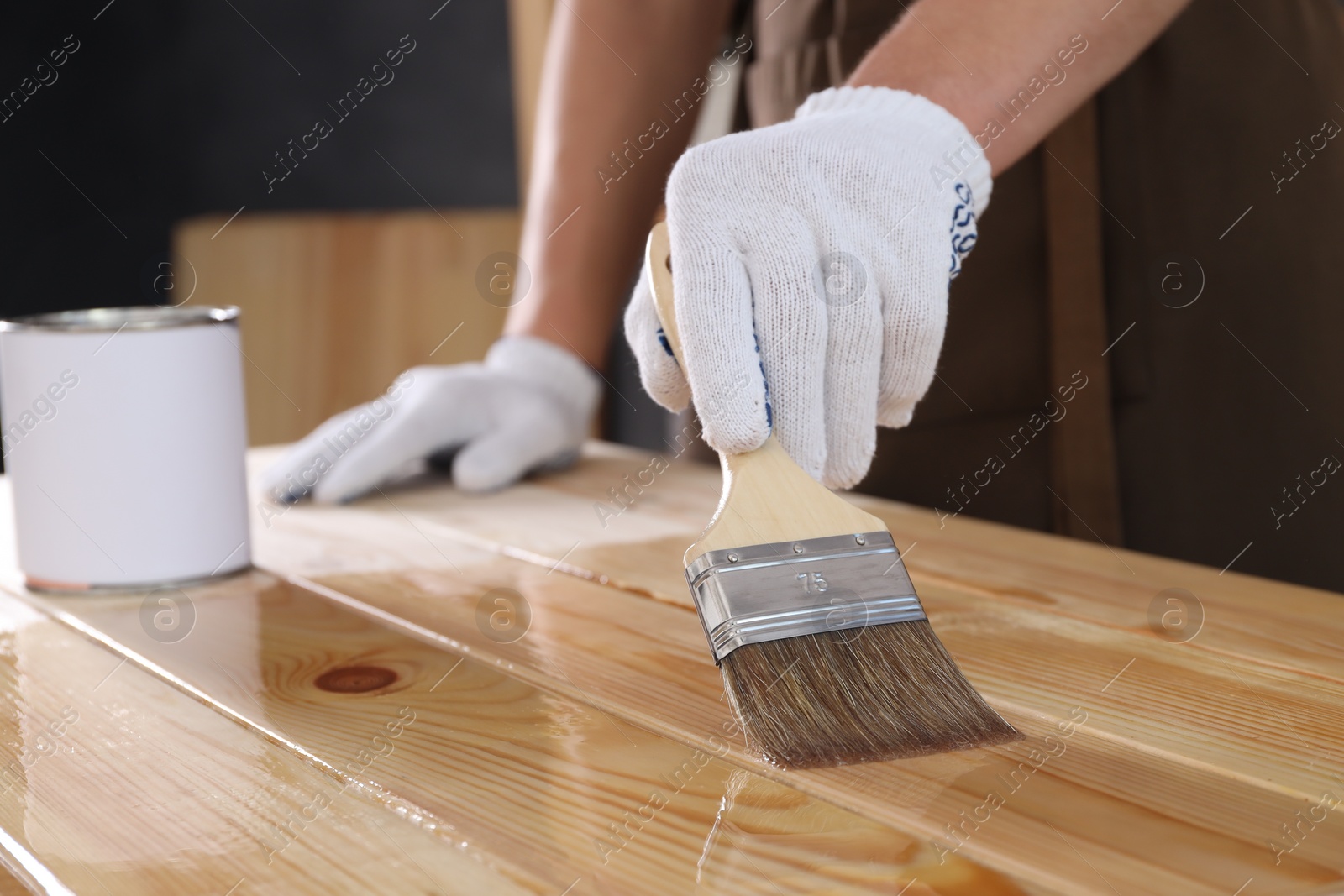 Photo of Man varnishing wooden surface with brush indoors, closeup