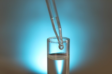 Photo of Dripping liquid from pipette into test tube on light background, closeup